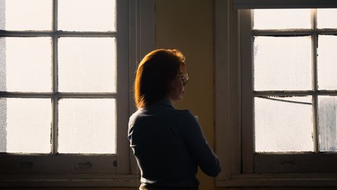 A thoughtful woman stands silhouetted against a frosted vintage window, evoking contemplation and solitude.