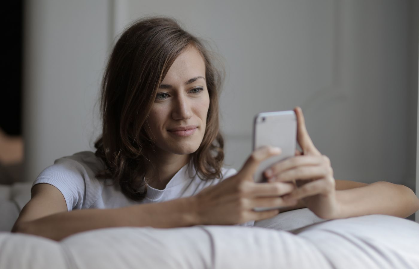 Woman comfortably sitting on a couch using her smartphone with a smile, enjoying leisure time indoors.