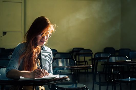 A focused young woman studies alone in a sunlit classroom, highlighting determination.