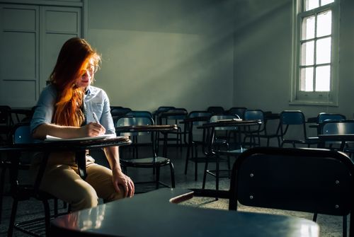 Free A solitary student reflects while writing in an empty classroom bathed in sunlight. Stock Photo