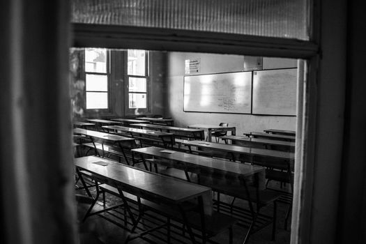 A deserted classroom with rows of benches and a whiteboard, captured in black and white.