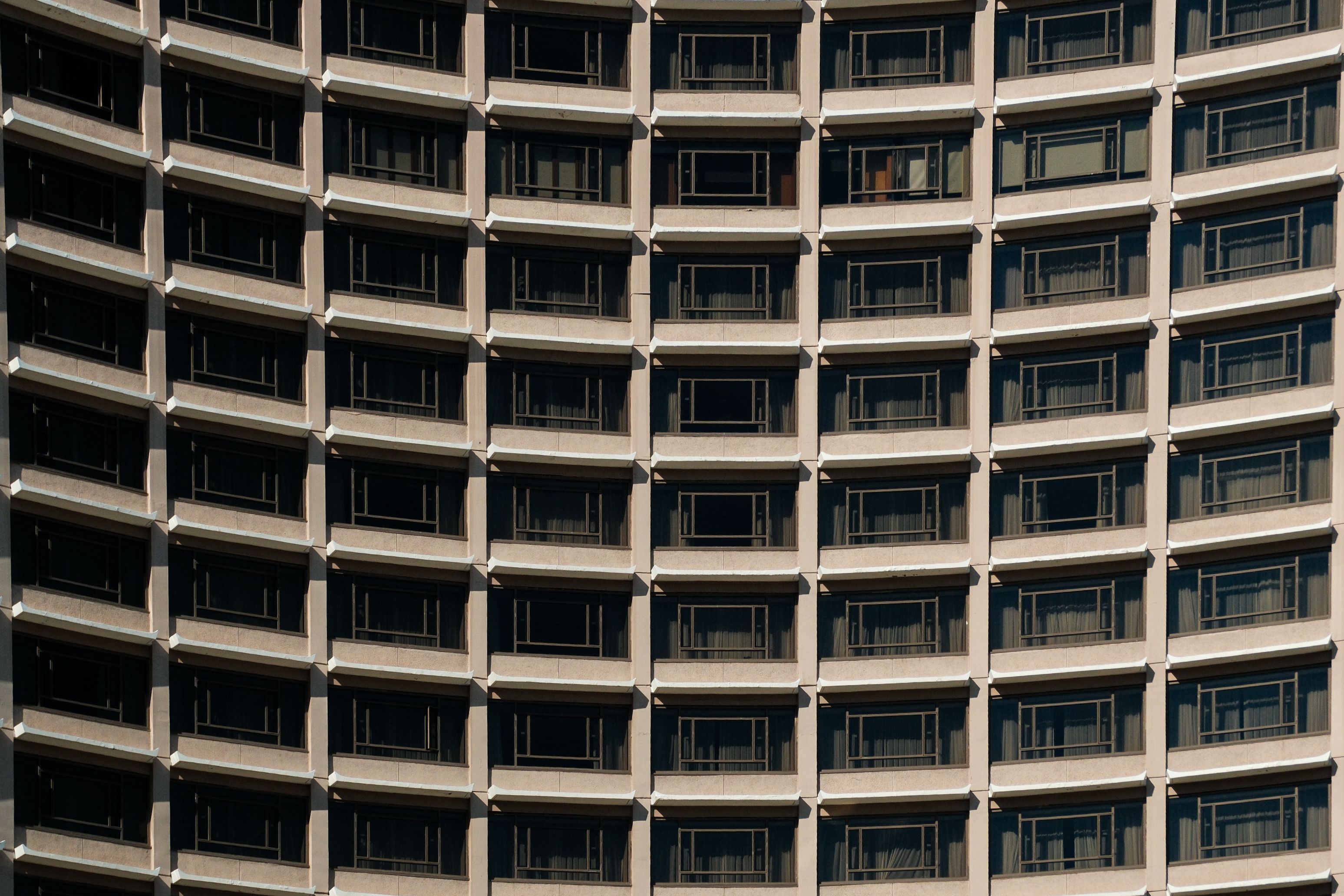 Urban high-rise building with curved facade featuring rows of balconies creating a repetitive pattern.