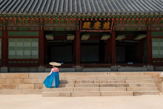 A person wearing Korean Hanbok stands in front of a traditional palace in Seoul, South Korea.