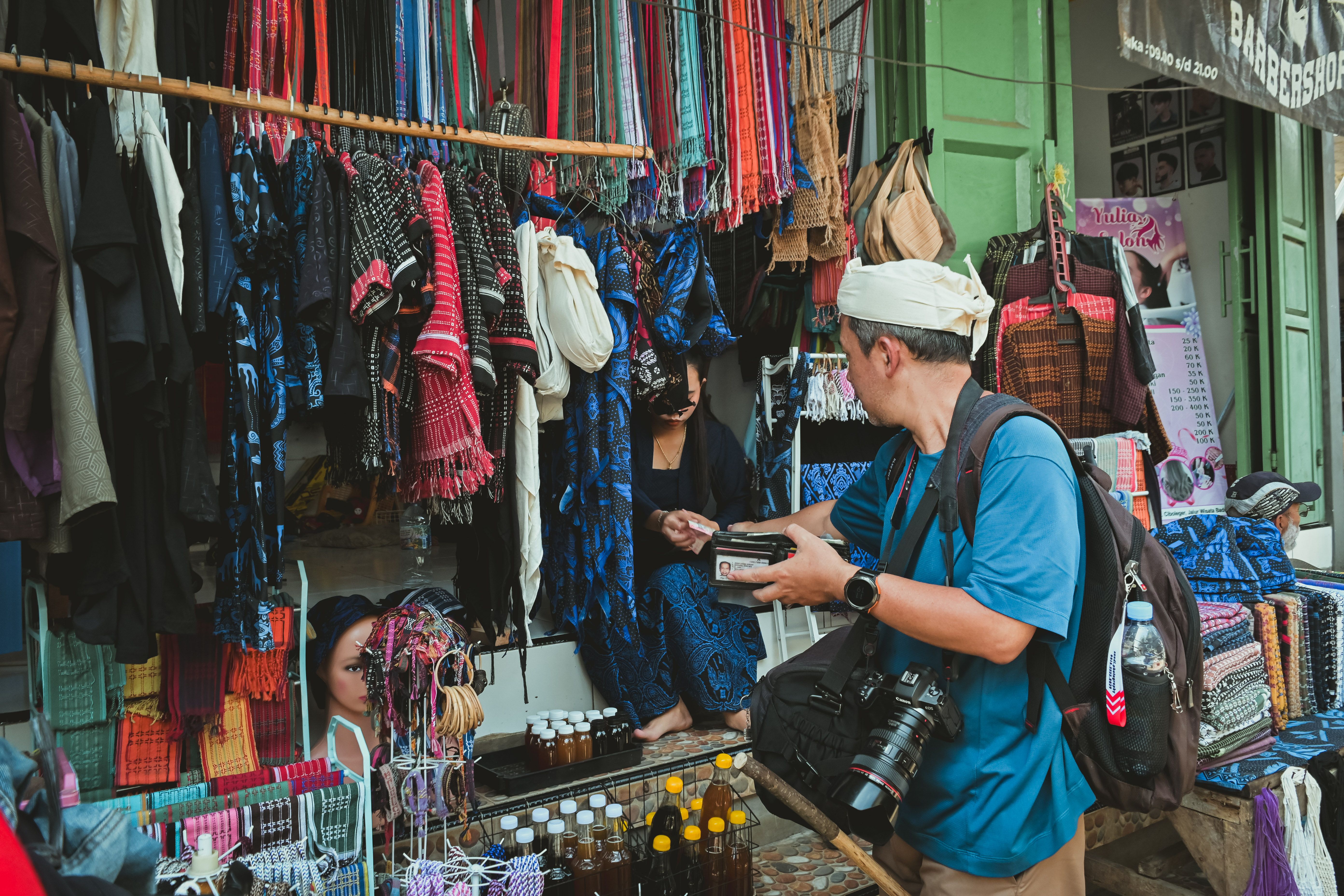 A shopper bargaining with a vendor over folded sarongs and woven bags at Sukawati Art Market in Bali