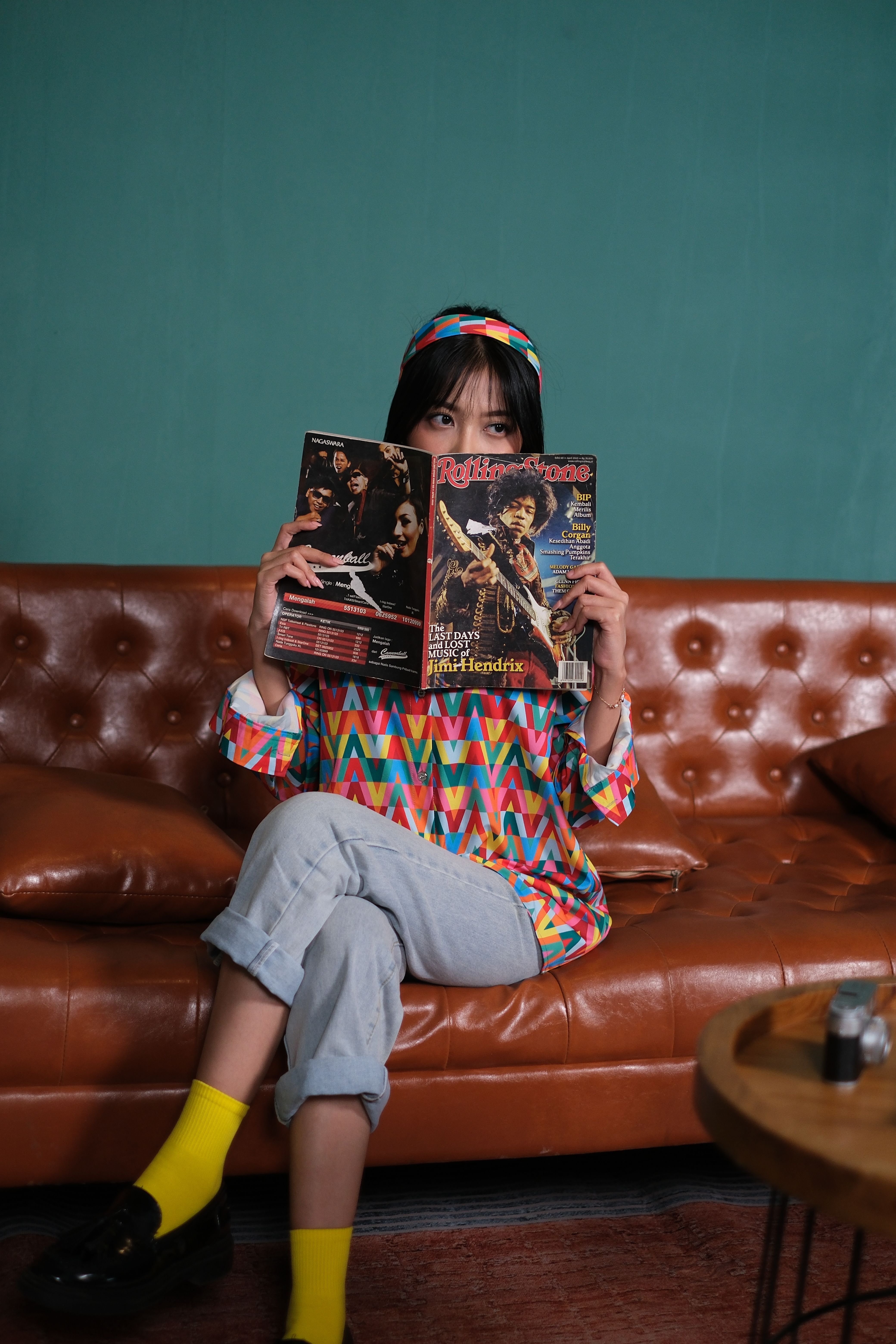 Colorful portrait of a woman reading a magazine on a vintage leather sofa, showcasing 70s fashion.