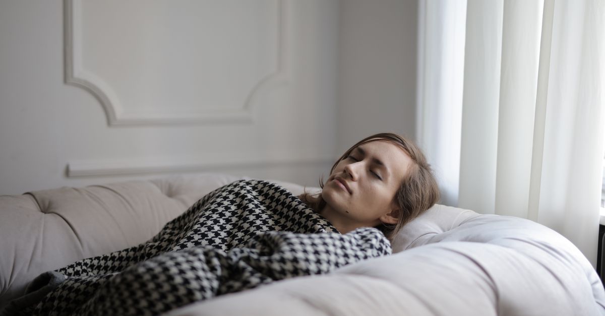A woman peacefully resting on a couch with a checked blanket, showcasing relaxation.