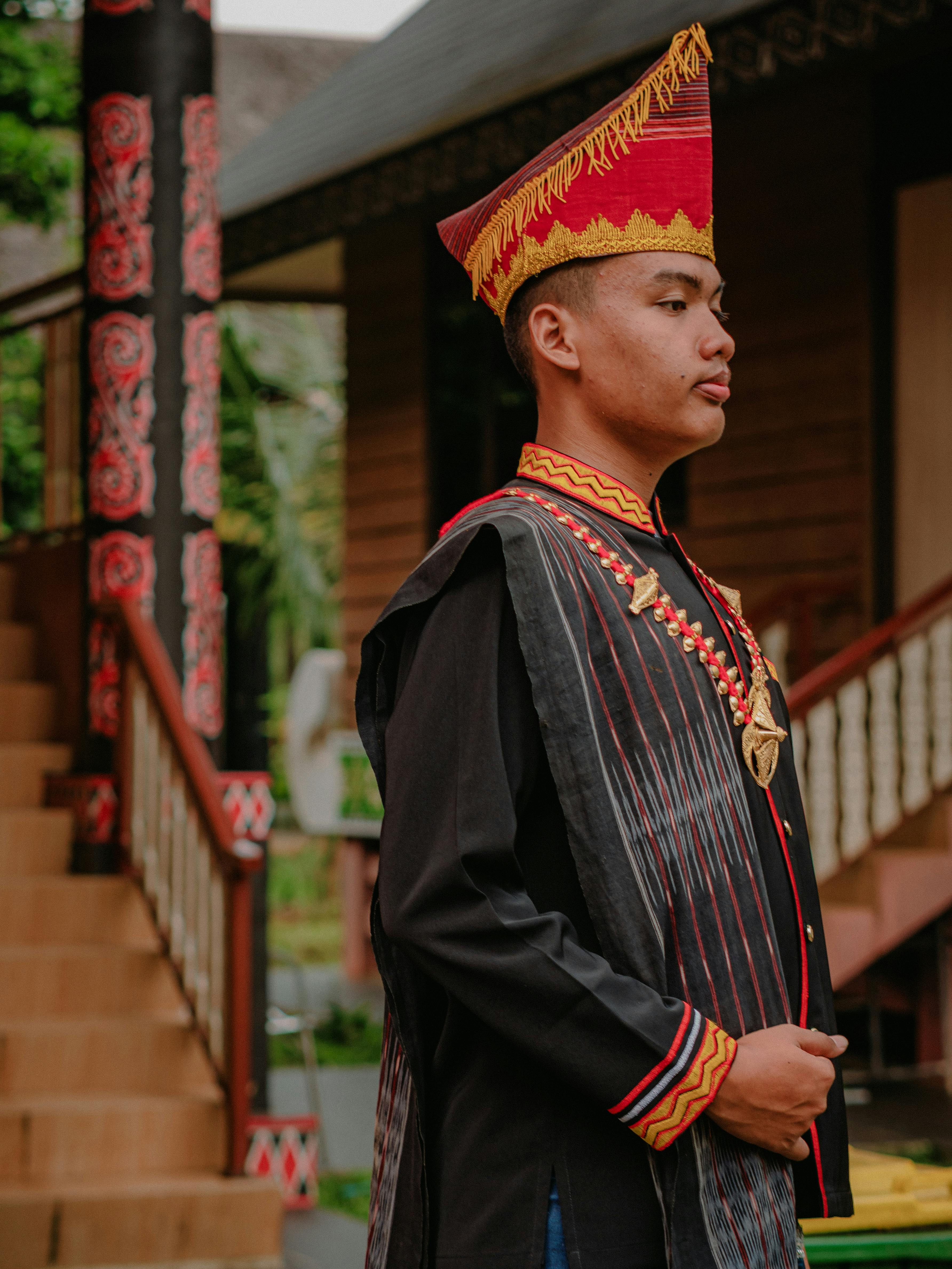 Man wearing traditional Indonesian attire in a cultural setting outdoors.