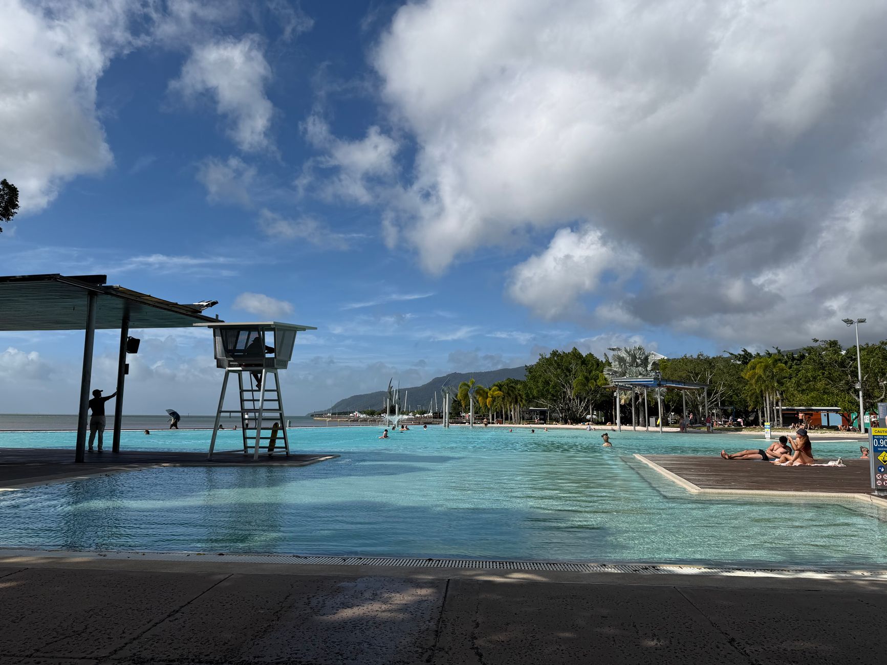 Dia ensolarado relaxante na Cairns Esplanade Lagoon com céus azuis claros e nadadores desfrutando da água.