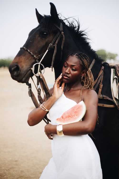 Free Stylish portrait of a young woman holding watermelon beside a horse in a rural setting. Stock Photo