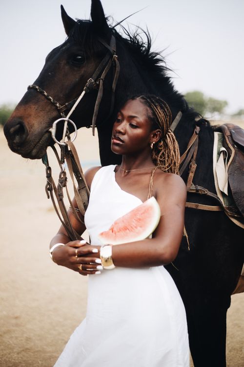 Free Stylish woman in white dress holding watermelon slice beside a horse. Stock Photo