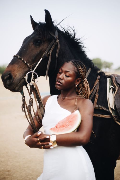 Free A serene scene with a woman in white holding a watermelon next to a horse. Stock Photo