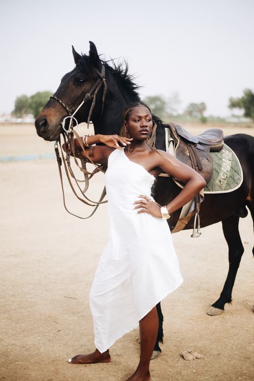 Free Elegant woman in white dress posing confidently with a horse in a sunlit outdoor setting. Stock Photo