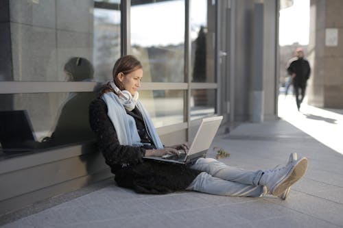 Woman in Black Coat and Gray Pants Sitting on Gray Concrete Floor