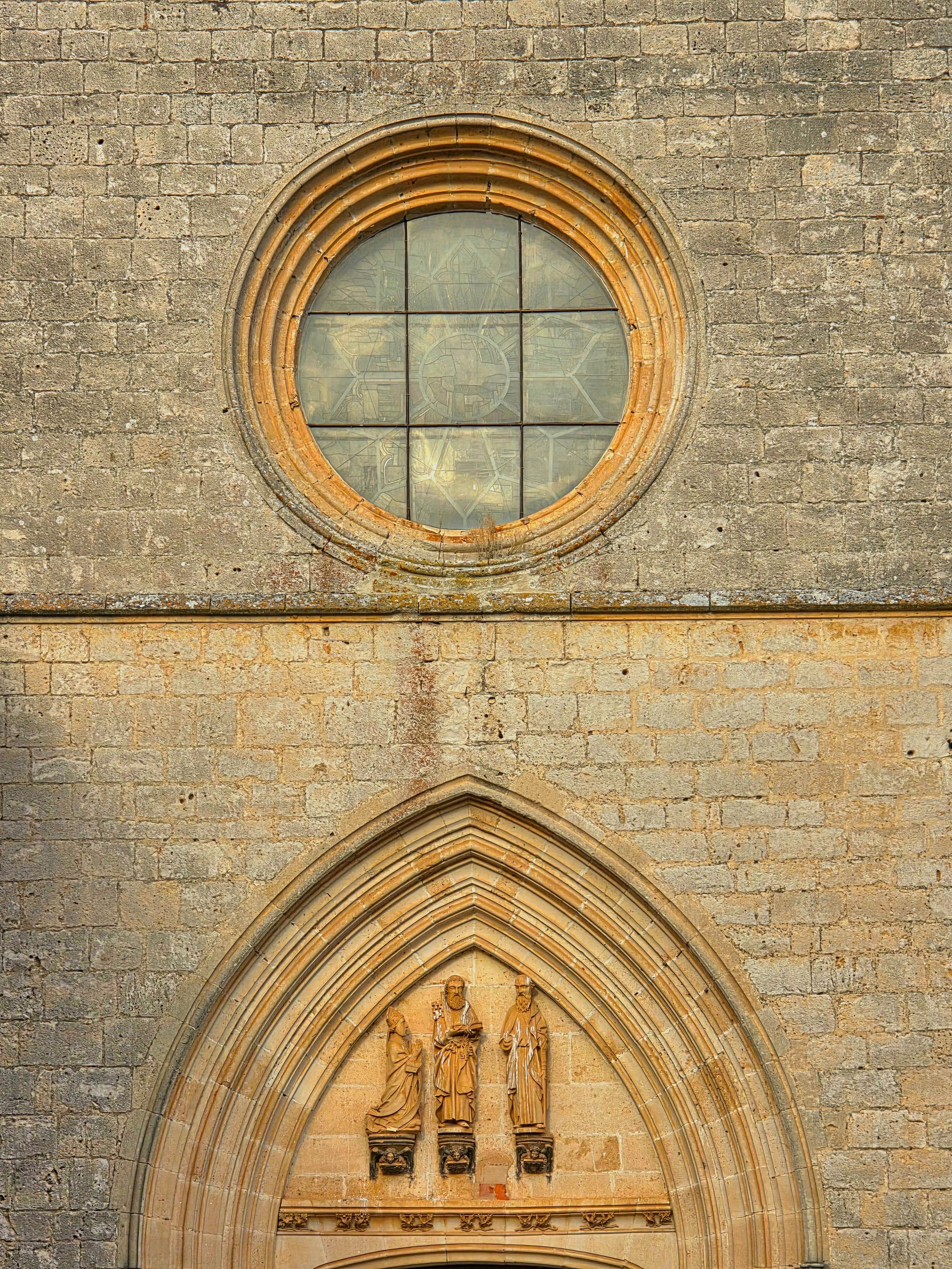 Close-up of Gothic architecture featuring a stained glass window and statues in Burgos, Spain.
