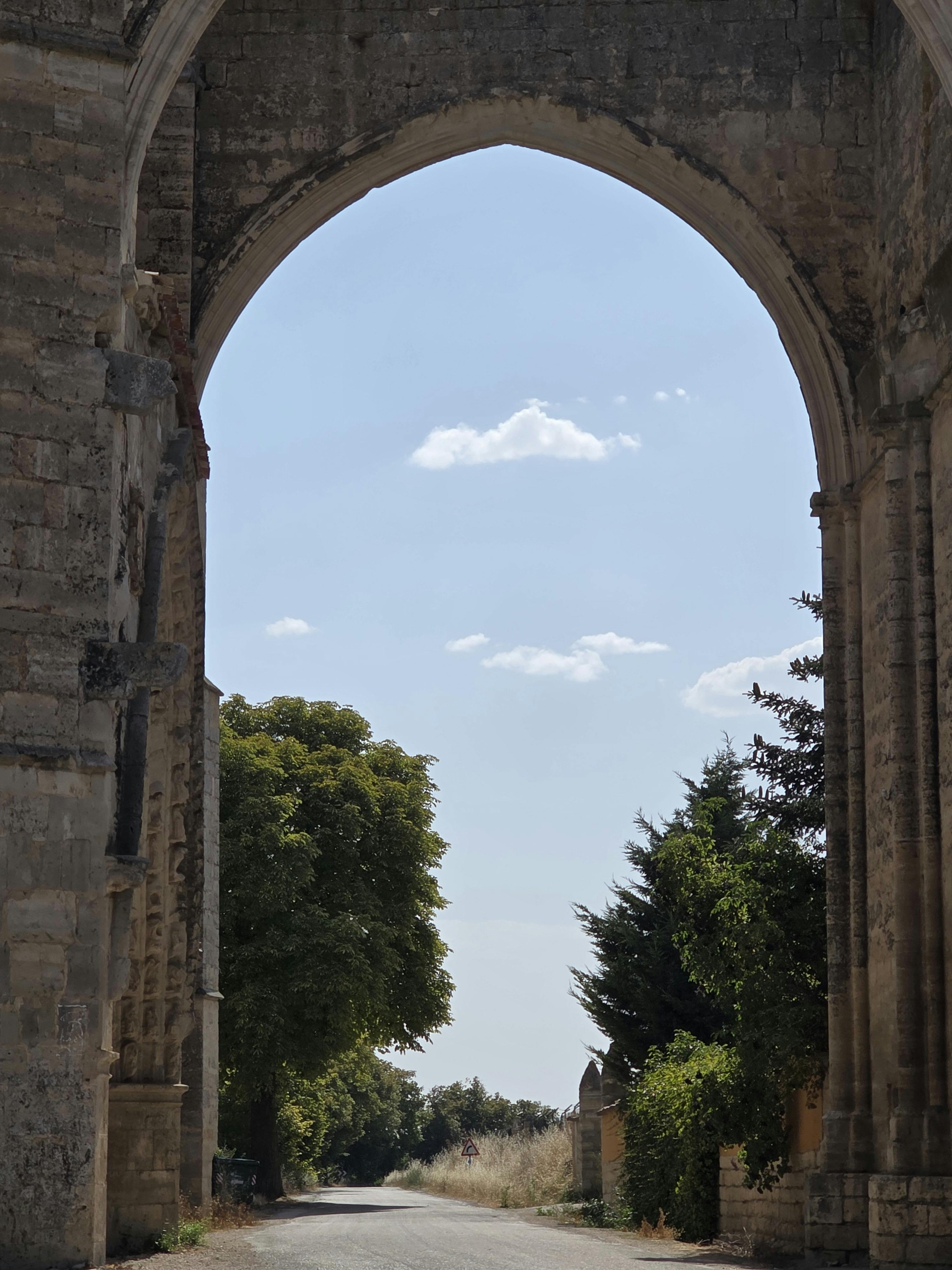 View of a historic arched stone gate with trees and blue sky in Burgos, Spain.
