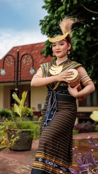 Young woman in ethnic attire plays a hand drum outdoors, showcasing cultural heritage. - Fotografer Sidoarjo
