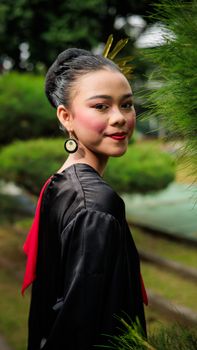 Elegant portrait of a woman in traditional attire standing outdoors with a vibrant garden backdrop. - Fotografer Sidoarjo