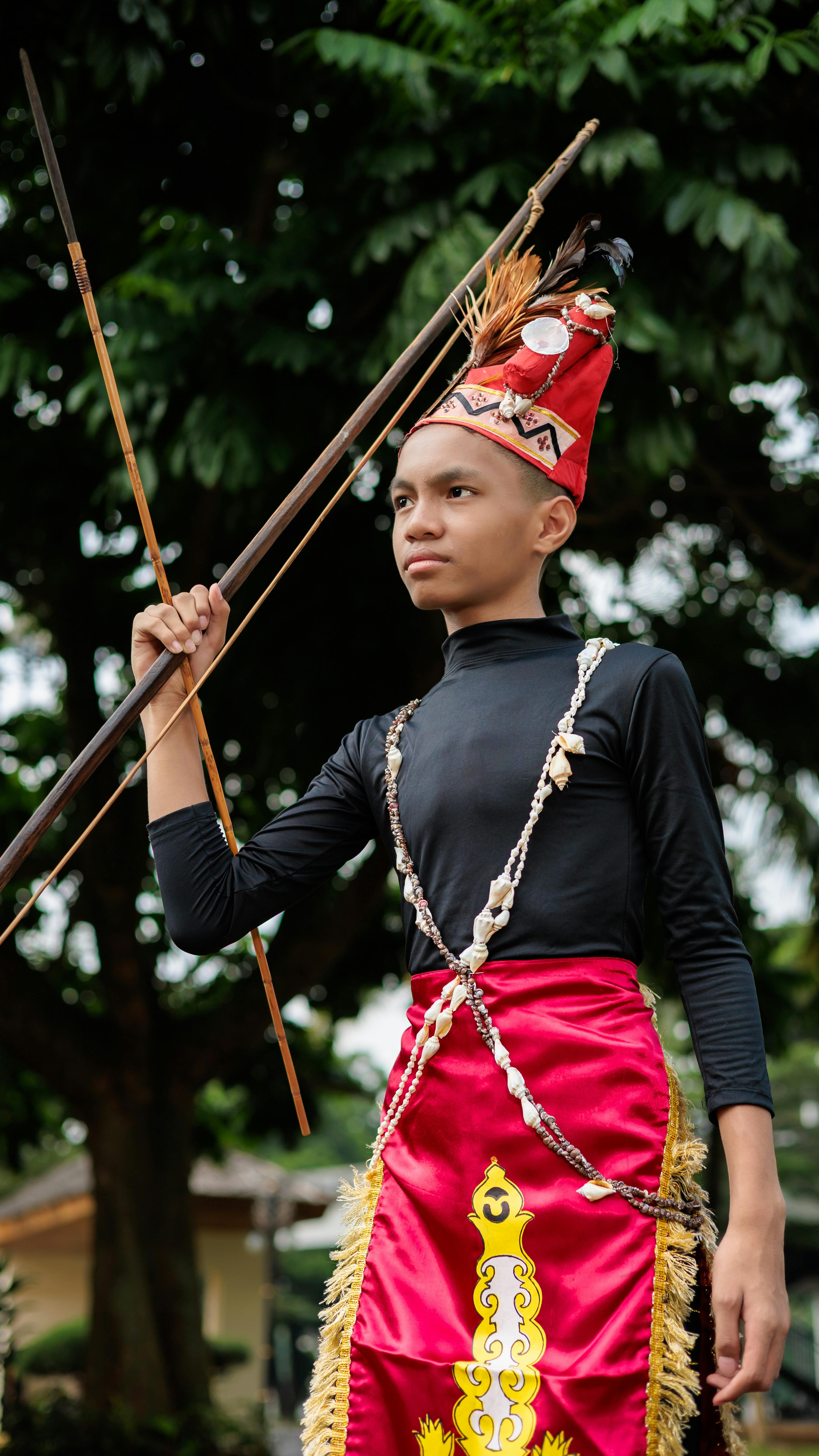 A young boy dressed in vibrant traditional attire holds spears outdoors, exuding cultural pride.