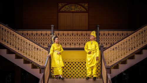 Free A couple in vibrant yellow traditional Malay attire on ornate stairs in Jakarta, Indonesia. Stock Photo