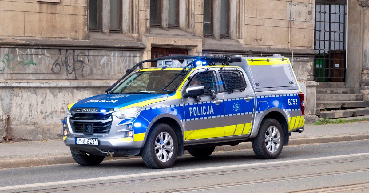 Blue and yellow police car parked on the street in Wrocław, Poland, beside an old building.