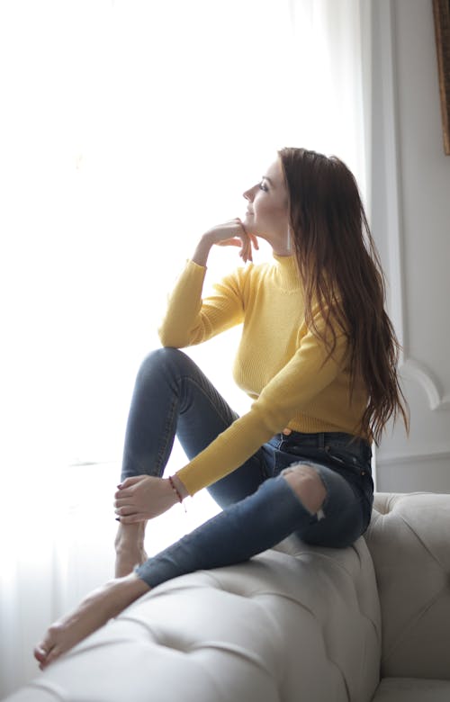 노란색 긴 소매 셔츠와 블루 데님 청바지 소파에 앉아있는 여자