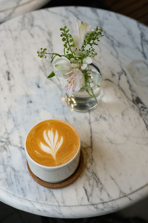 Free Cappuccino with latte art beside elegant floral vase on marble table at a cafe in Istanbul. Stock Photo