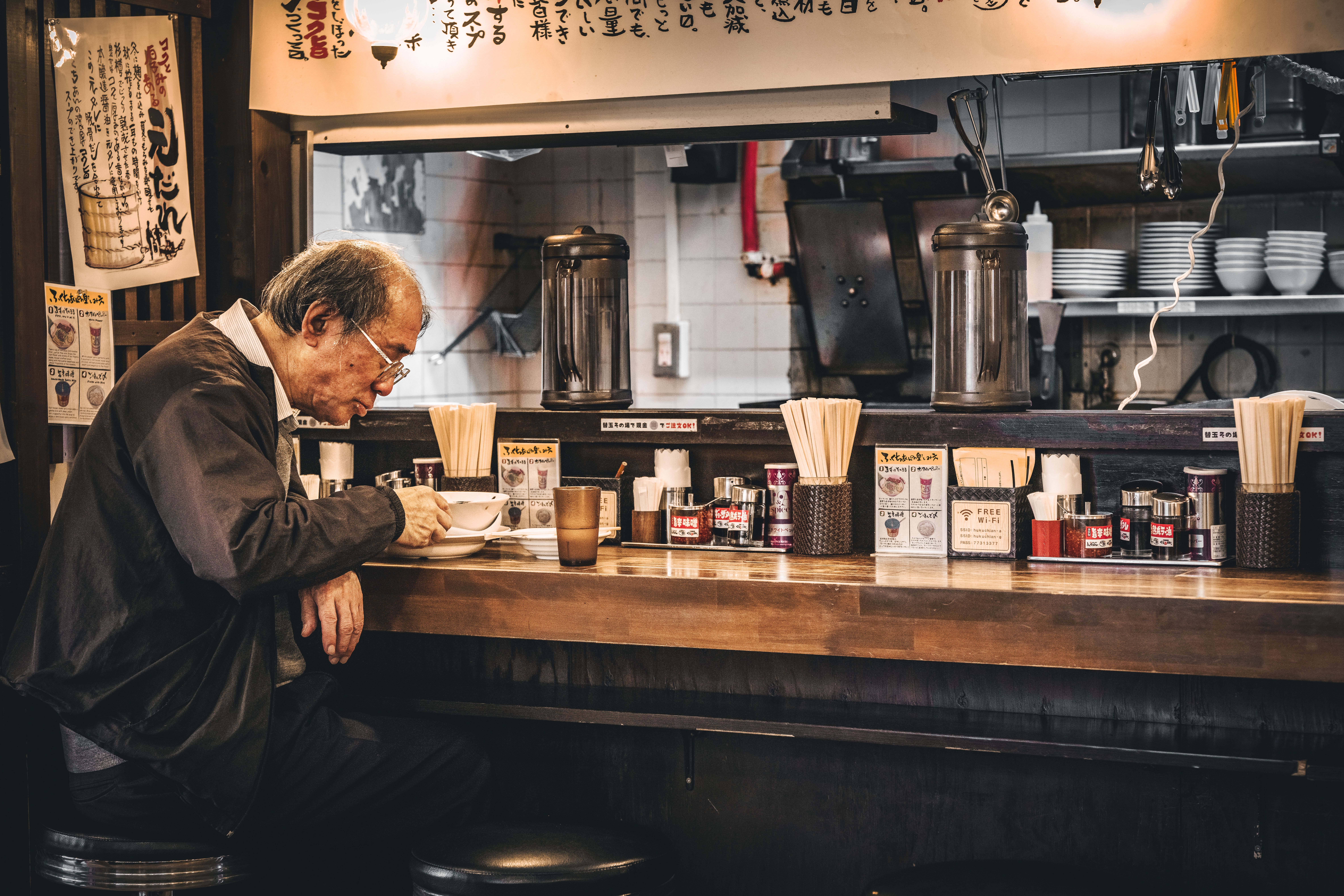 高齢の男性が東京の伝統的なラーメン店で一人で食事をし、日本料理を堪能している。