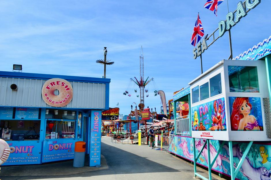 A vibrant amusement park scene with colorful rides and food stands under a clear sky.