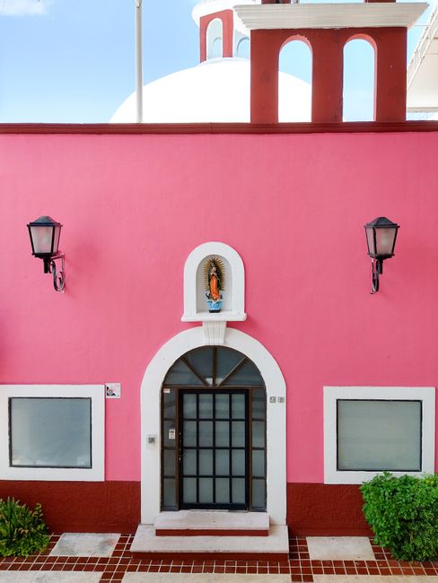 Colorful pink facade with a Virgin Mary shrine featured in colonial architecture. Captured in Cancún, Mexico.