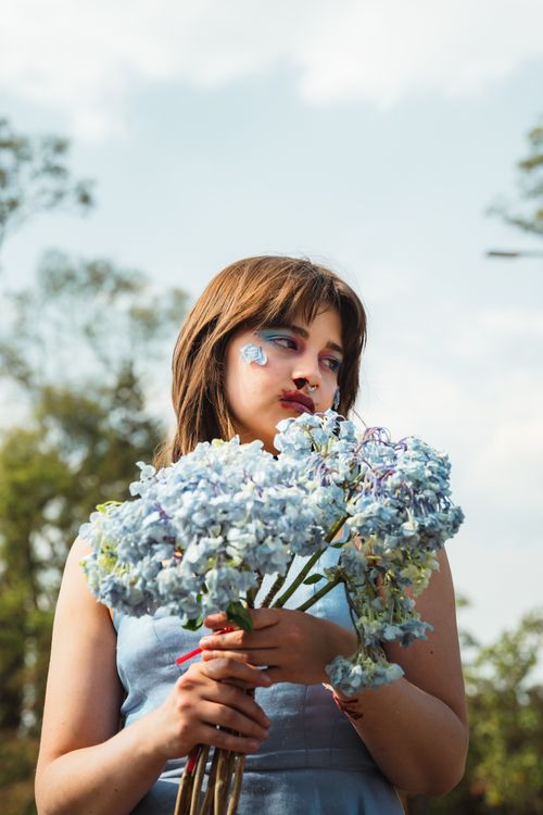 Free Portrait of a young woman holding blue hydrangea flowers outdoors with a serene expression. Stock Photo