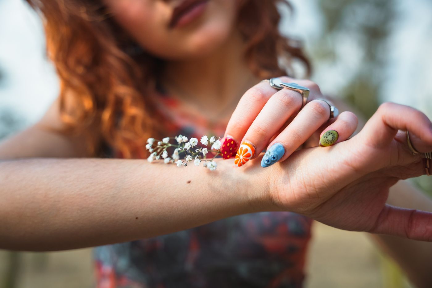 Mano con nail art ilustrado de frutas y flores, manicura artística en tonos cálidos