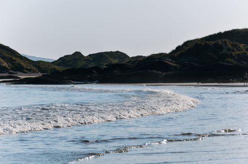 Free Serene view of waves on a sandy beach with lush hills in Ireland’s backdrop. Stock Photo