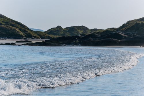 Free Serene coastal scene in Ireland with gentle waves and distant hills under a clear sky. Stock Photo
