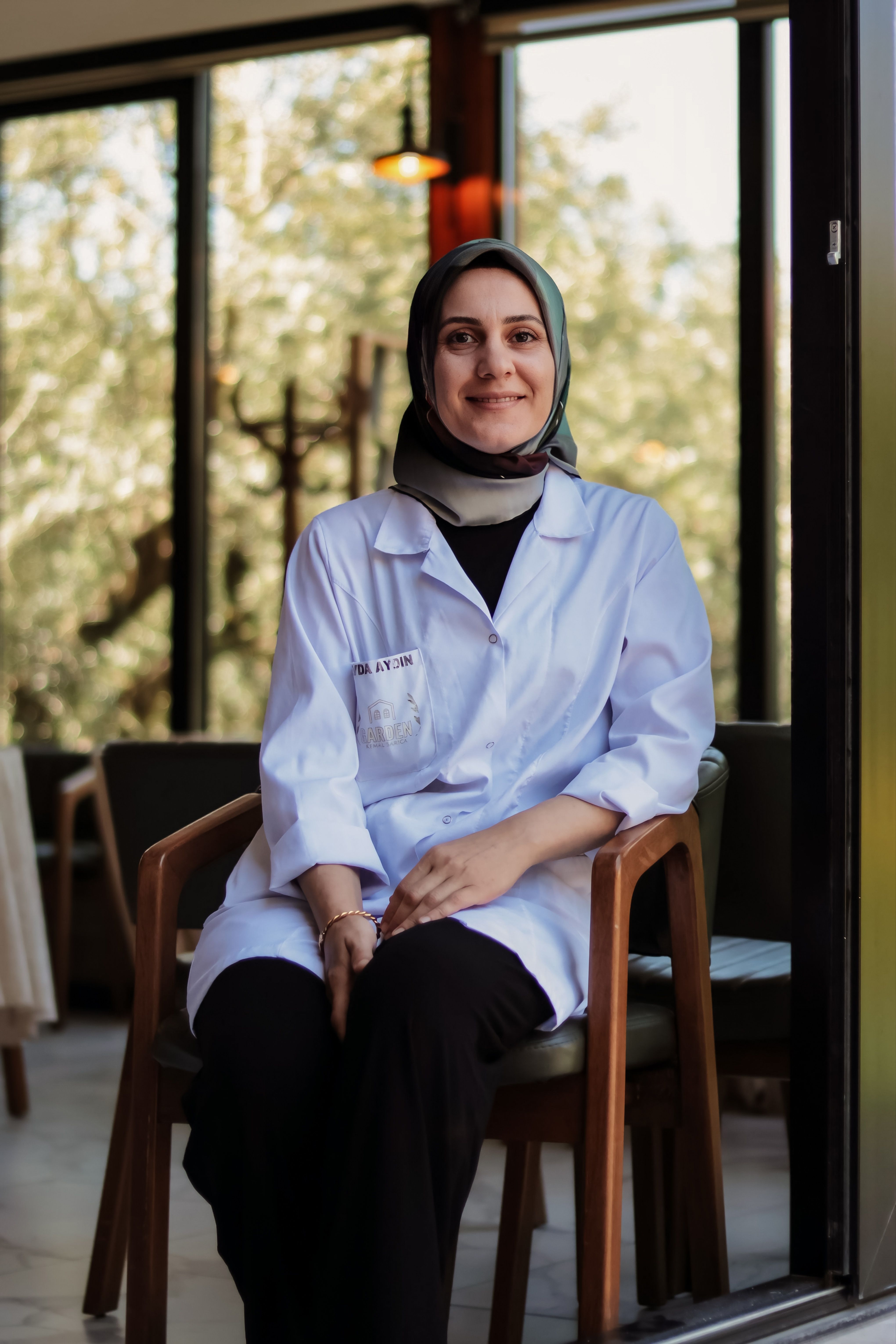 A smiling female scientist in a lab coat poses inside a bright room.