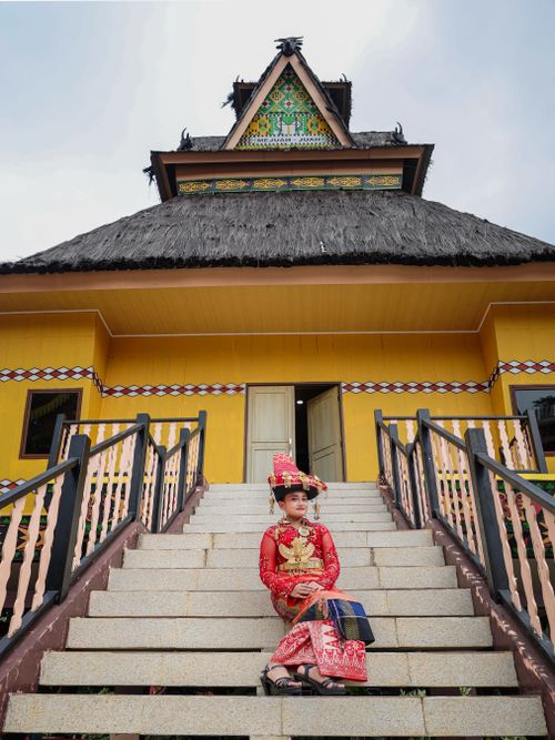 Free Woman in traditional attire sits on steps of a cultural building, showcasing vibrant heritage. Stock Photo