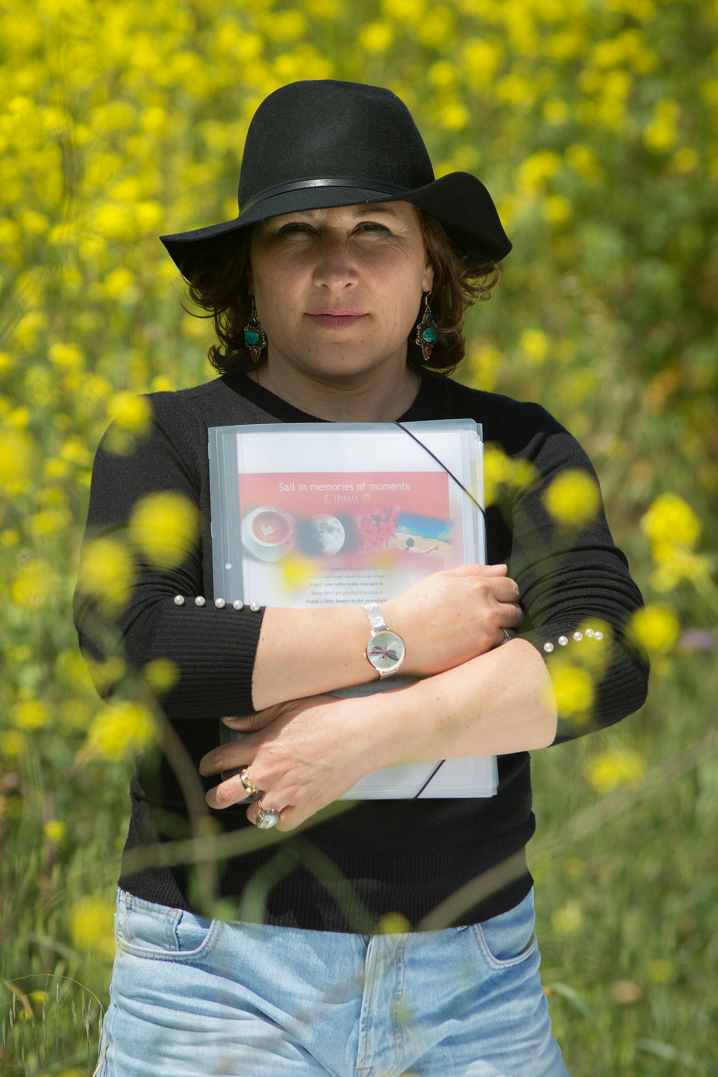 Woman in casual clothes holds a document outdoors in a field with yellow flowers.