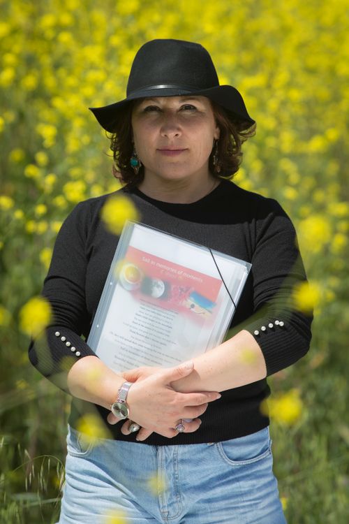 Free Woman in a field of yellow flowers holding a magazine, wearing a black hat. Stock Photo