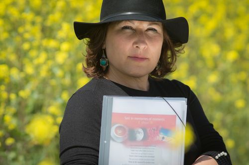 Free Portrait of woman in black hat holding a booklet in a yellow flower field. Stock Photo