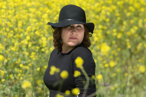 Free A woman wearing a black hat poses among vibrant yellow flowers in a sunny field. Stock Photo
