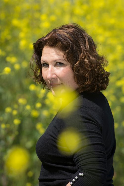 Free A woman in a black outfit stands amidst a vibrant yellow wildflower field, looking back. Stock Photo