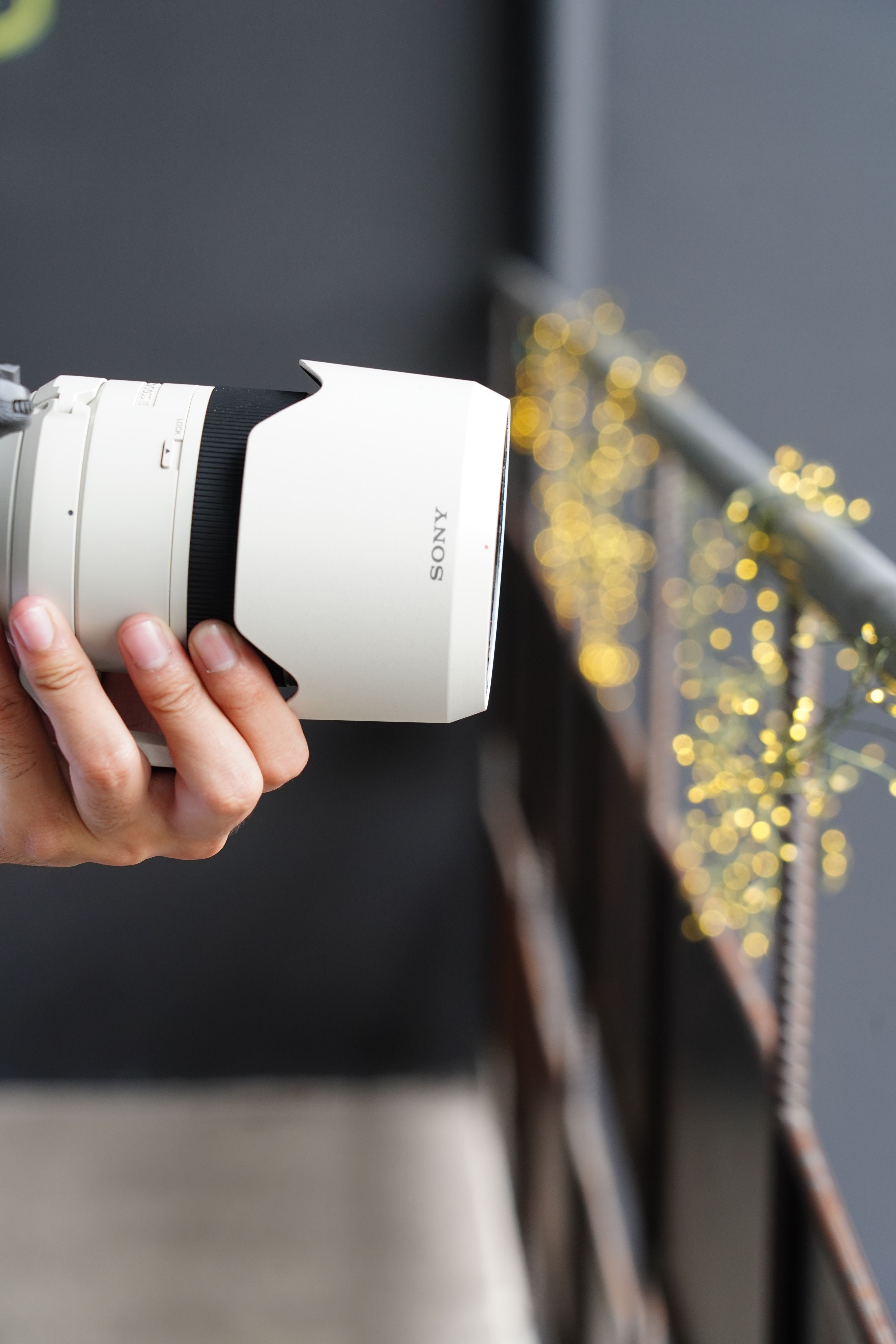 A close-up view of a hand holding a camera lens, with bokeh lights in the background.