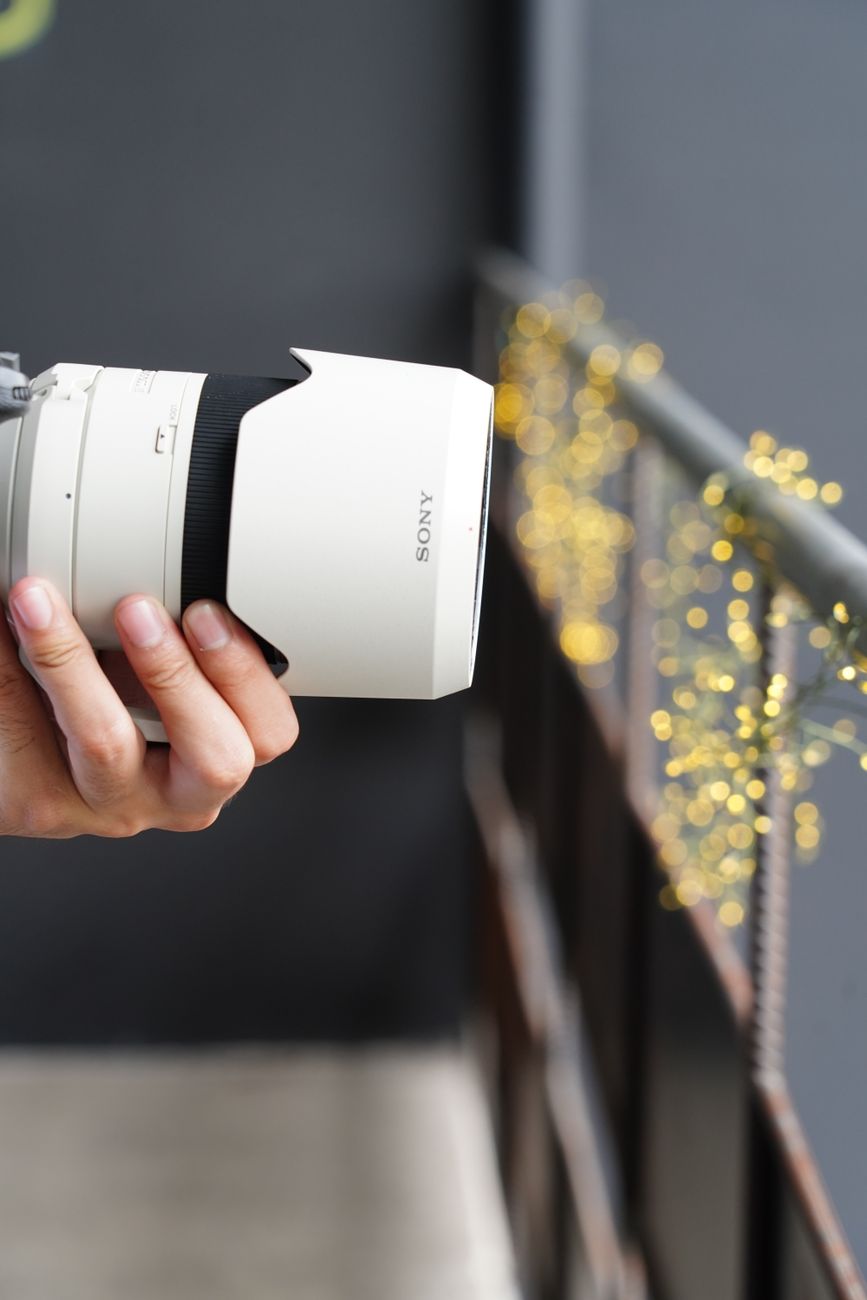 A close-up view of a hand holding a camera lens, with bokeh lights in the background.