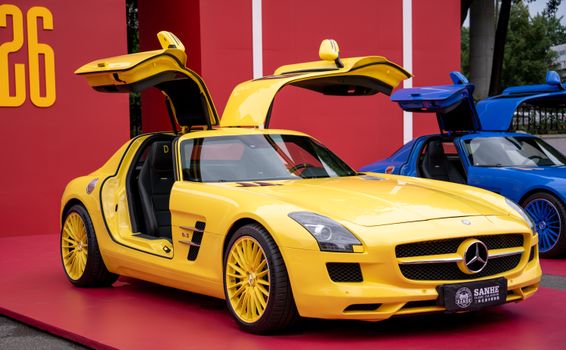 Yellow sportscar with gullwing doors open, showcasing its design at an outdoor auto exhibition.