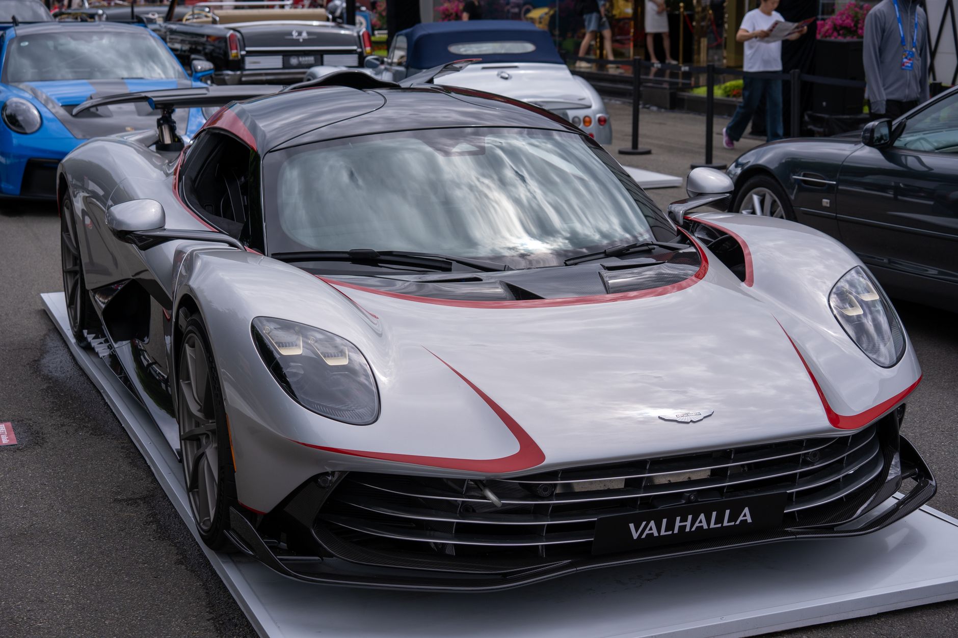 A sleek Aston Martin Valhalla showcased at an outdoor auto exhibition, surrounded by other luxury cars.