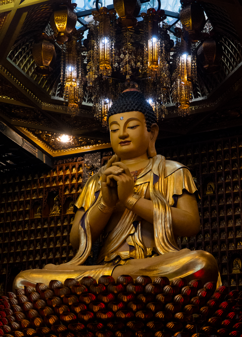 Free Majestic golden Buddha statue inside an ornately decorated temple with warm lighting. Stock Photo