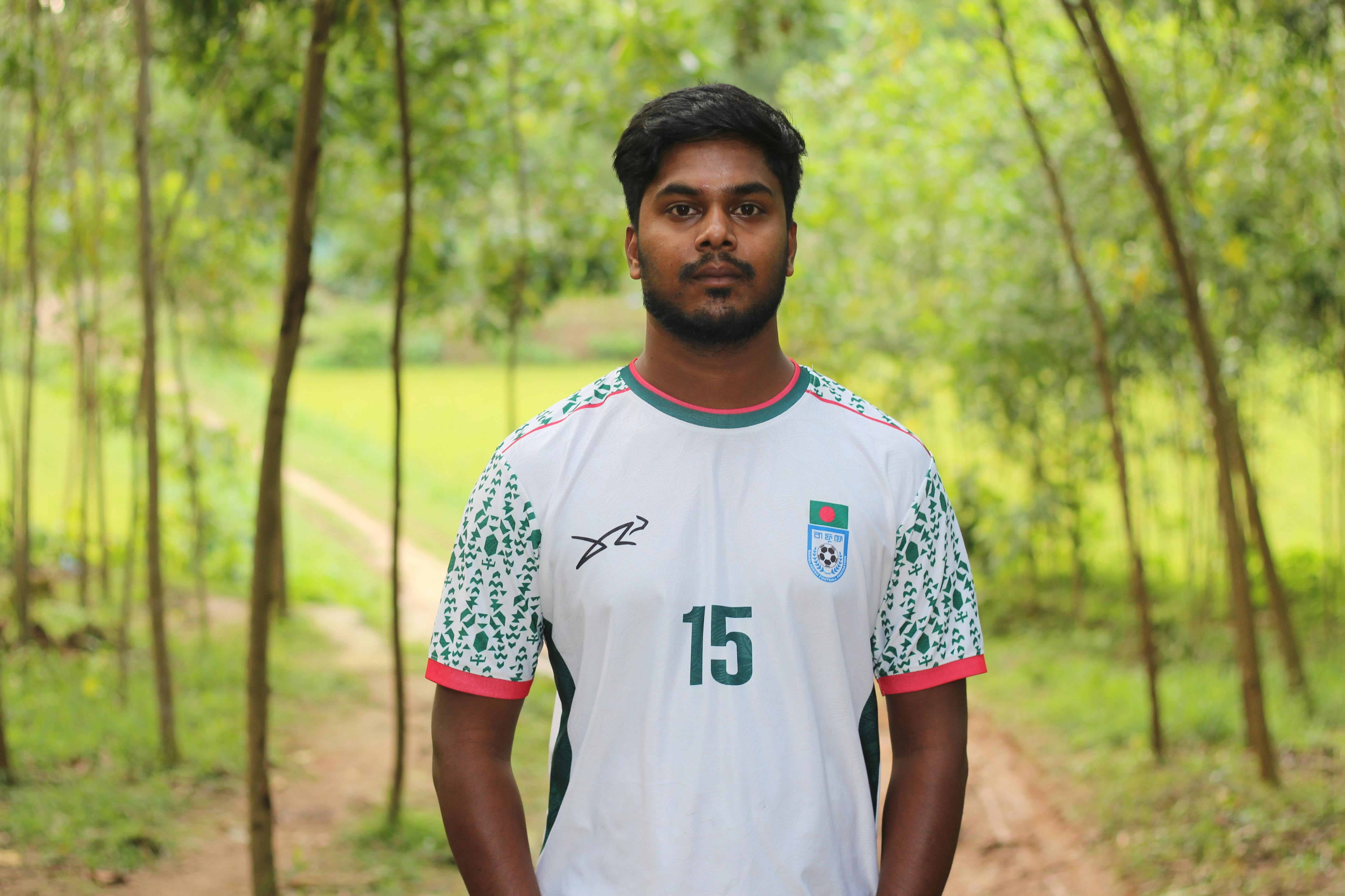 Young man standing in a natural setting, wearing a soccer jersey with the number 15.
