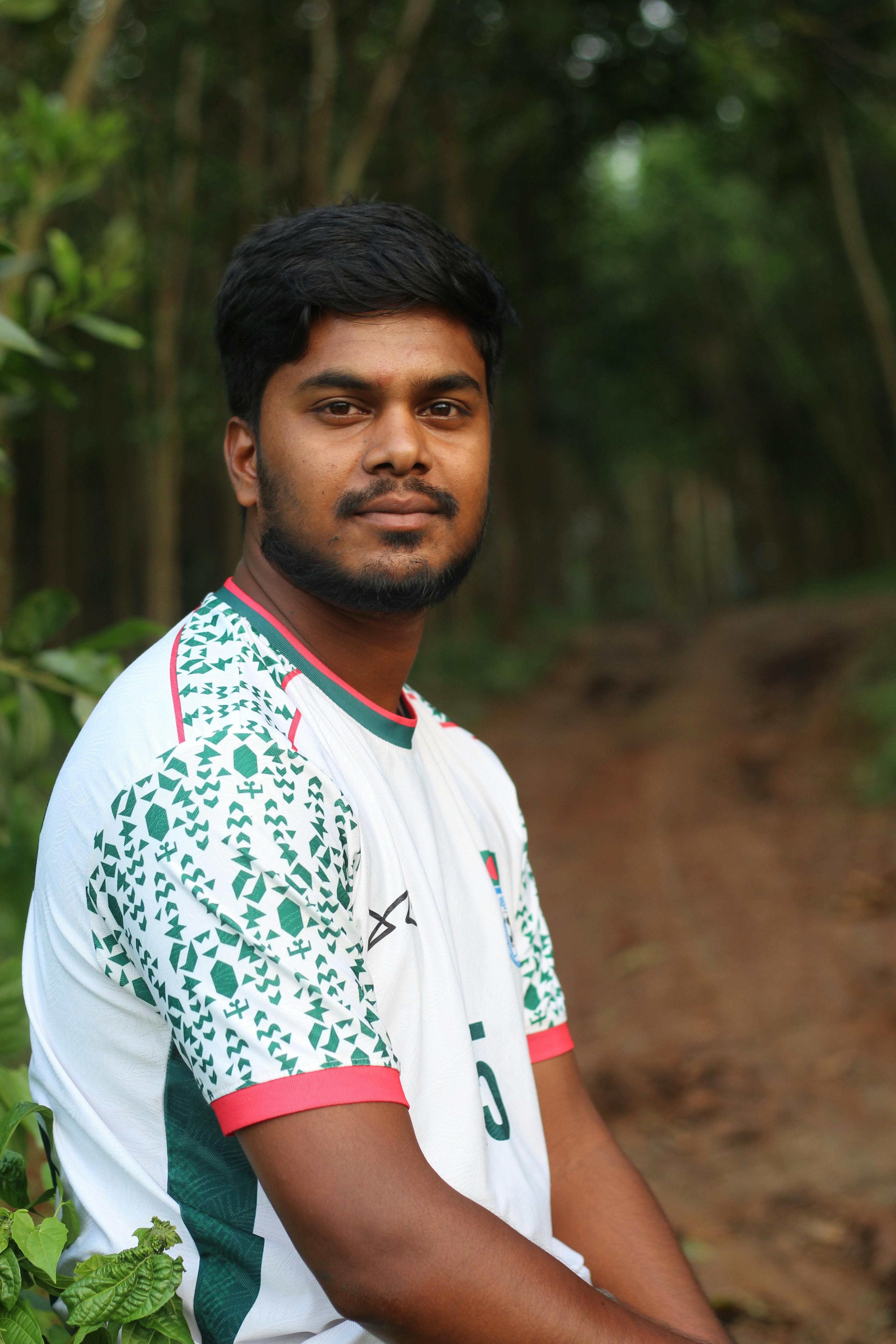 Young man in a sports jersey posing outdoors in a forest setting.