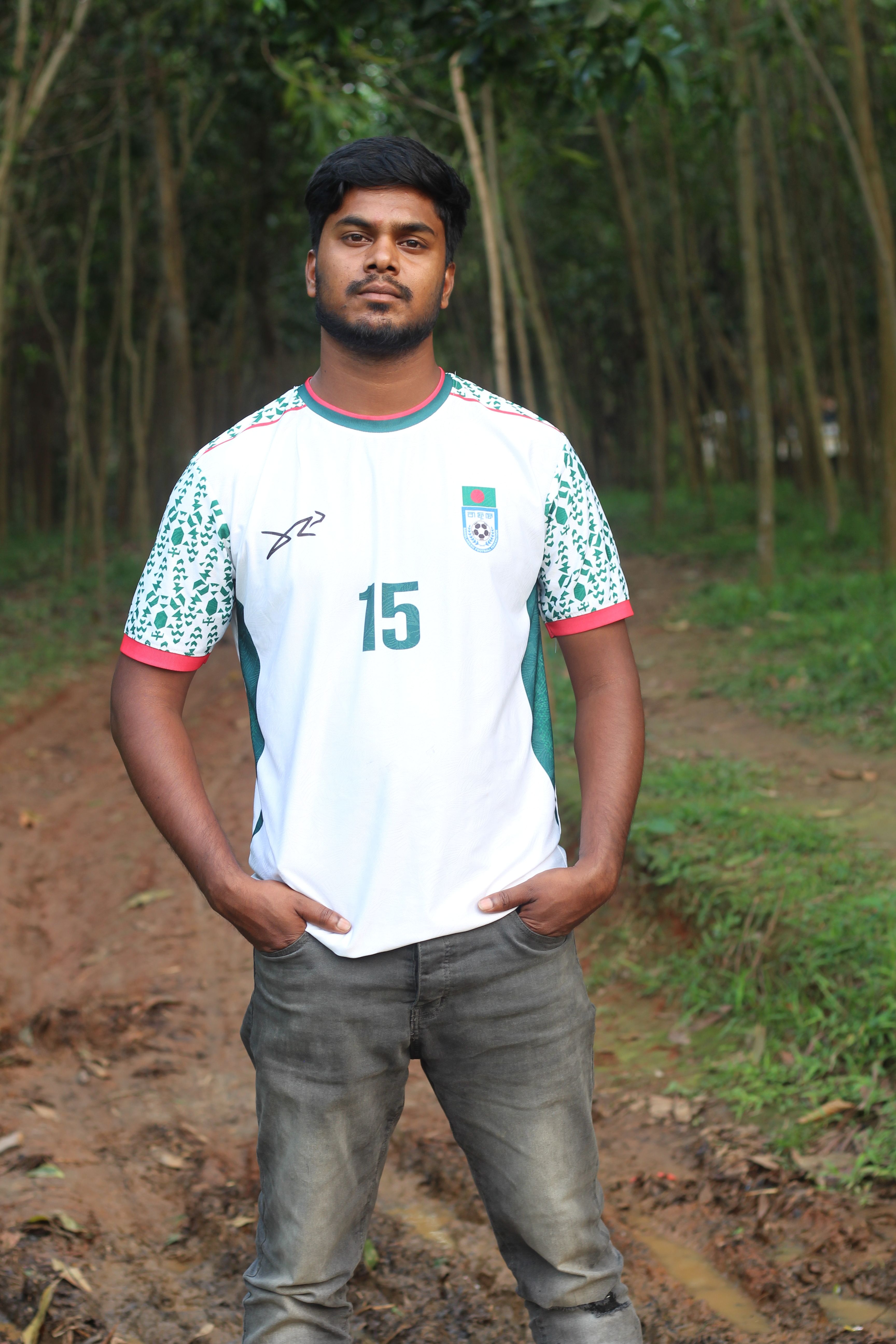 Man posing in a soccer jersey on a rural outdoor path.