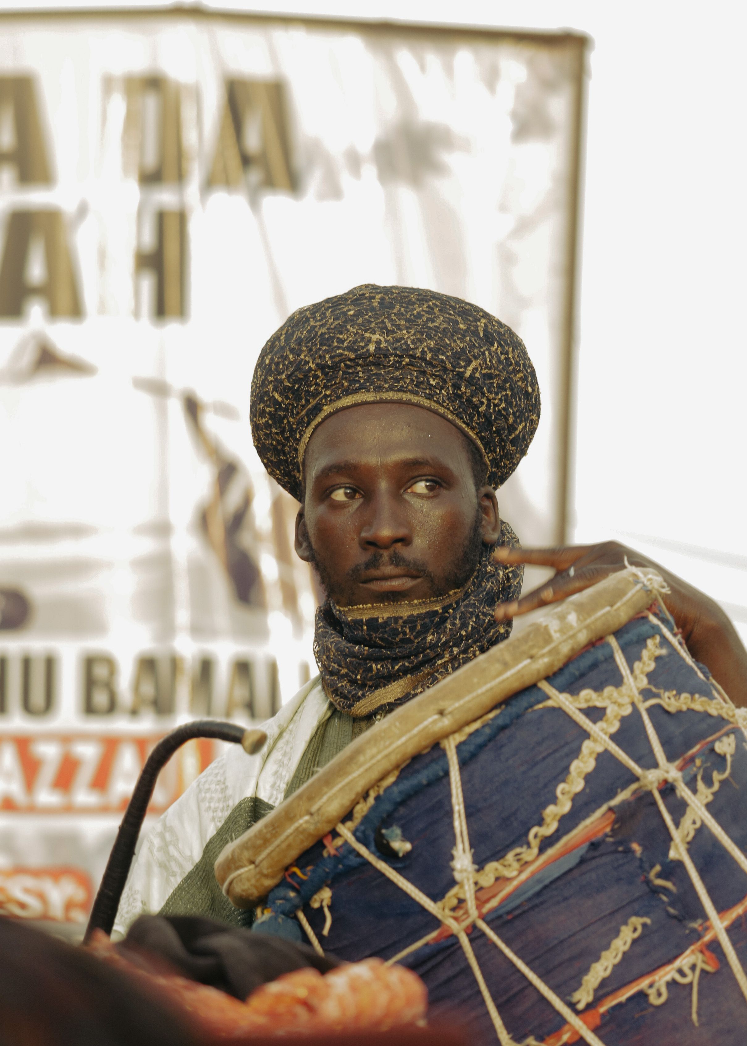African musician in traditional attire playing a drum, showcasing cultural music.