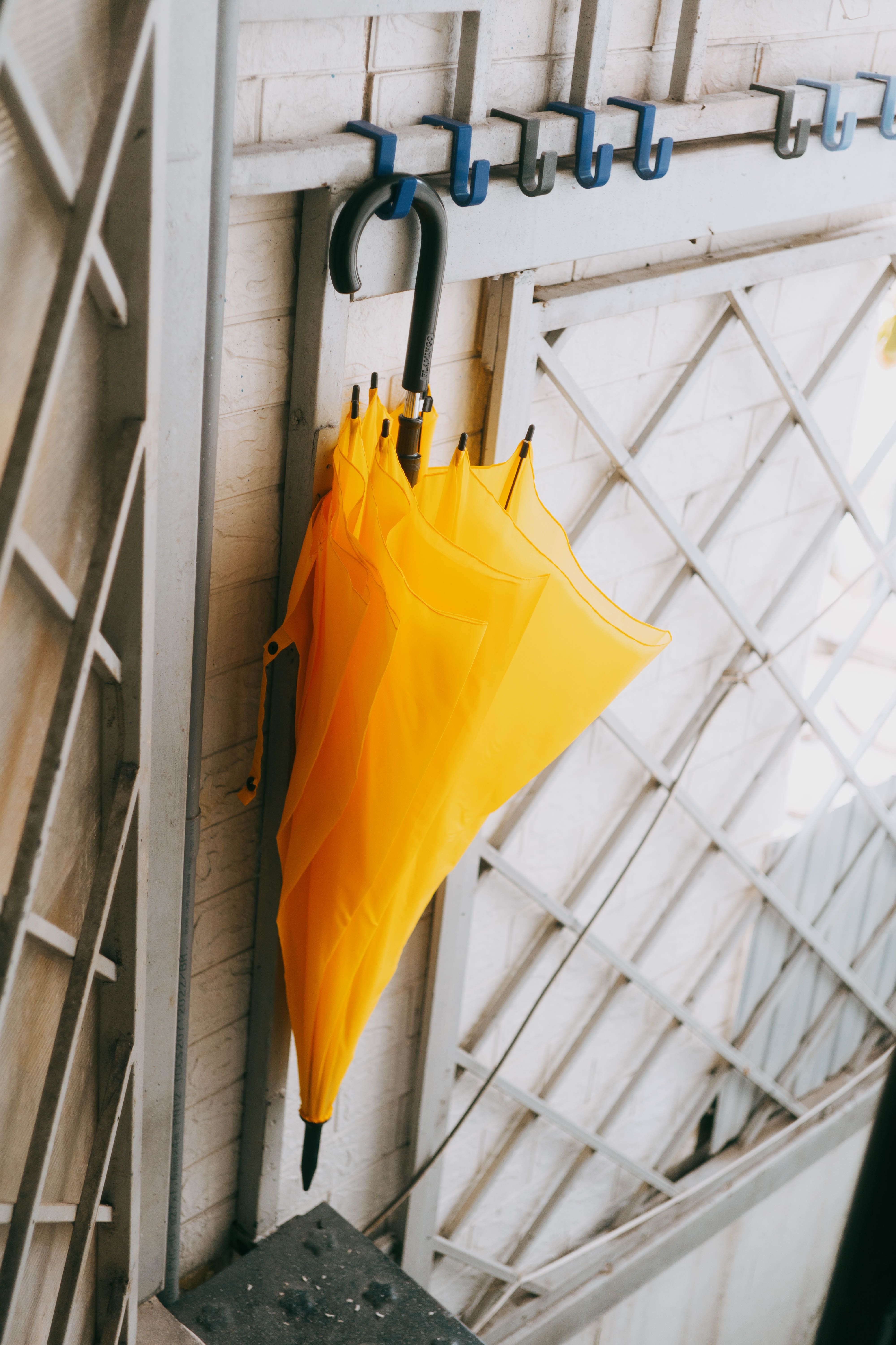 A yellow umbrella hangs on a metal rack against a rustic wall, creating a vibrant indoor composition.